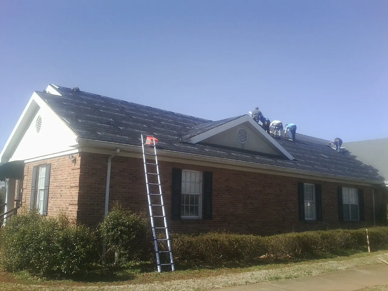 Crew tearing shingles off a brick ranch roof with a ladder set — Emergency Roof Repair work by our crew in Bon Secour