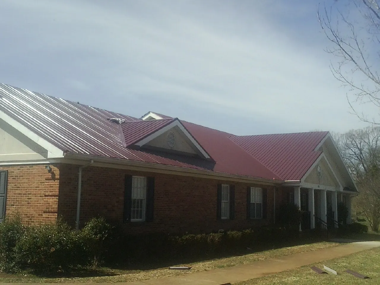 Red metal roof with gabled entries on a long brick building, from a Hail Damage Roof Repair job in Bon Secour