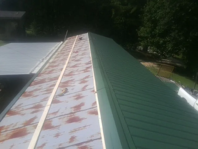 Old rusted panels beside newly installed green metal roofing — Wind Damage Roof Repair by Roofing Brothers in Bon Secour