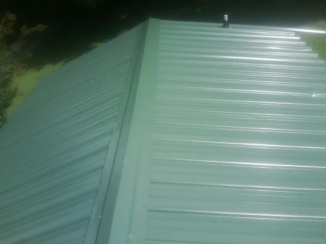 New green metal panels meeting at the ridge of a roof — Flat Roof Repair work by our crew in Bon Secour