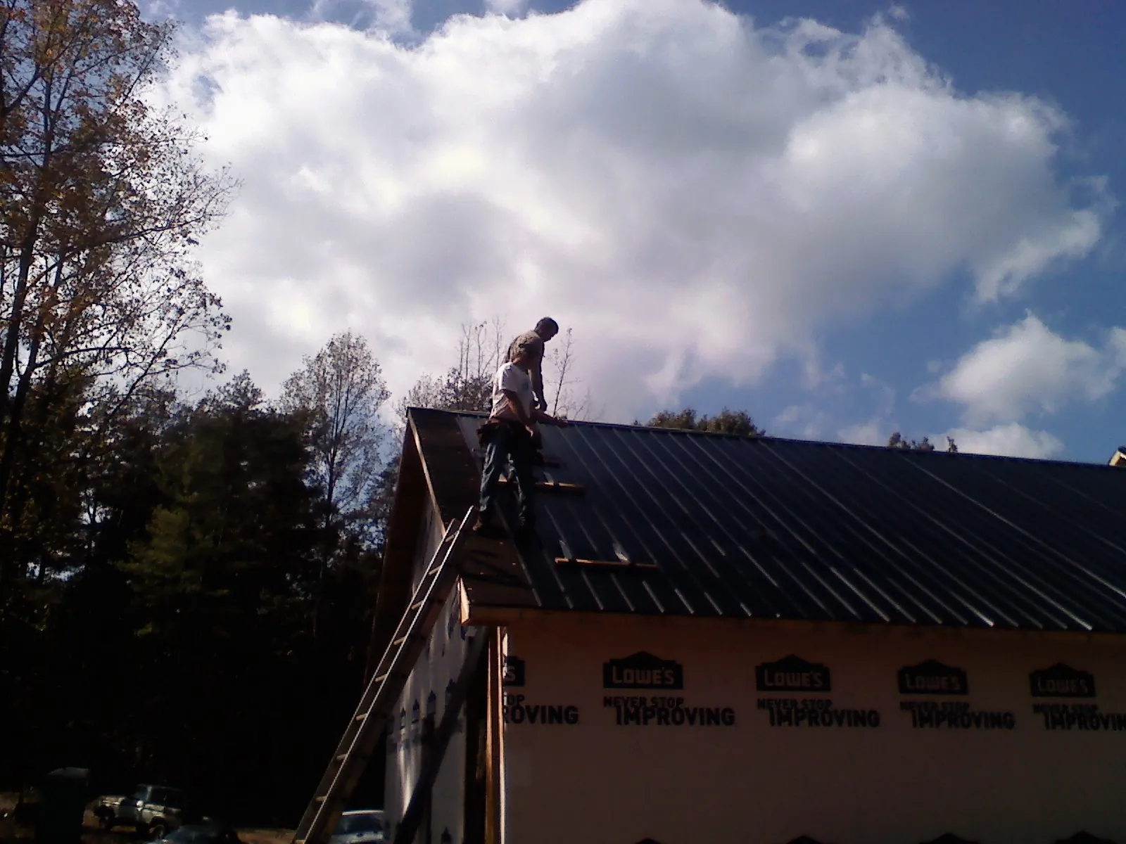 Roofer fastening dark metal panels high against a cloudy sky, from a Roof Inspection job in Bon Secour