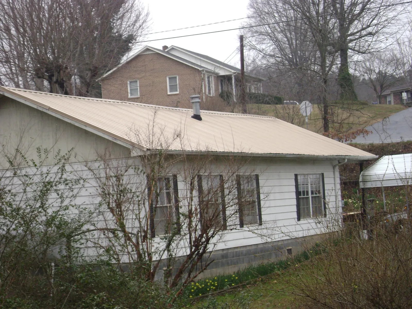 Tan metal roof on a white sided house set into a hillside — Commercial Roofing by Roofing Brothers in Bon Secour