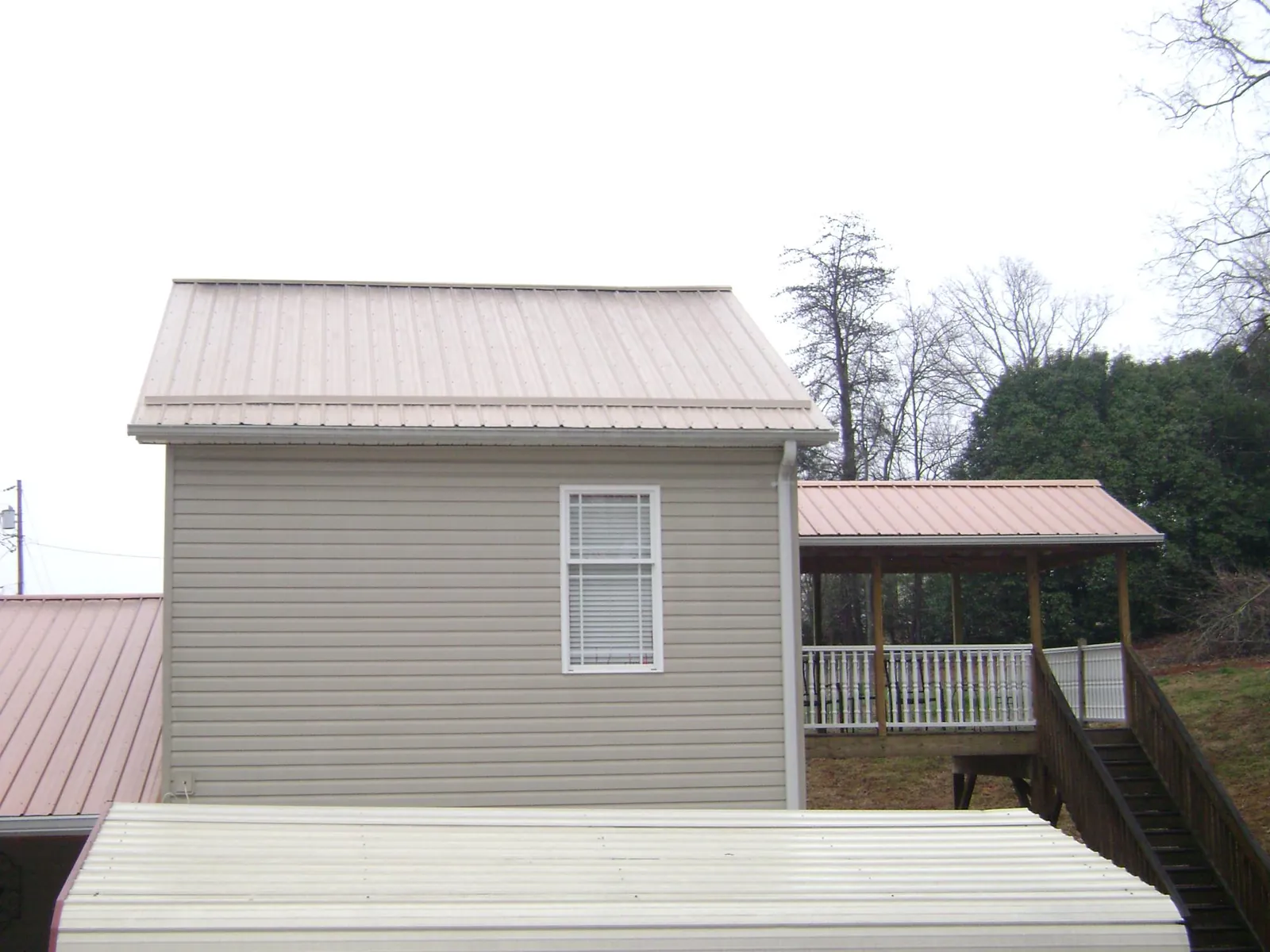 Tan metal roofs on a two story addition and attached porch, from a Roof Replacement job in Bon Secour